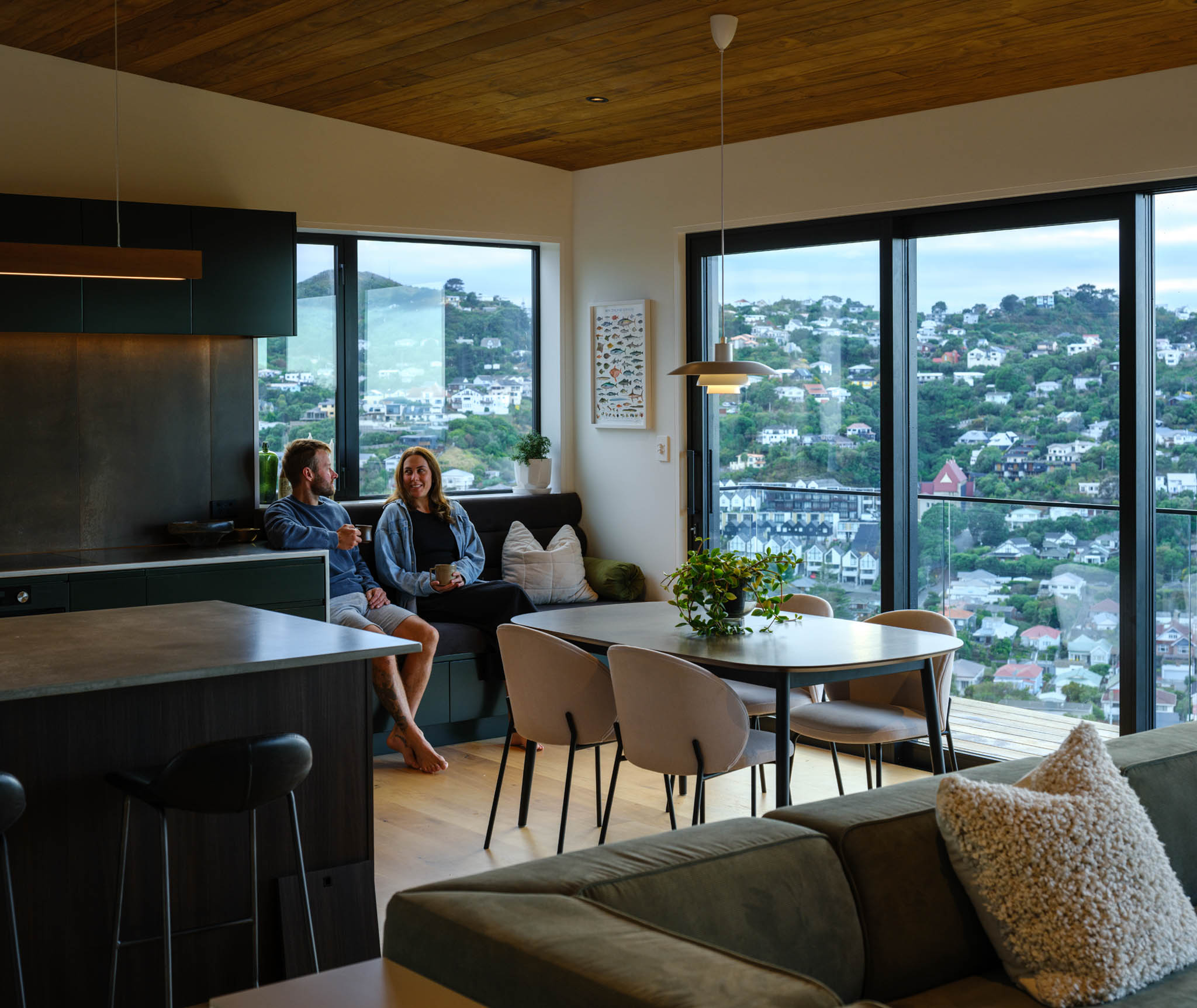 Couple sitting on a built-in bench seat in their kitchen with large windows overlooking Wellington.jpg